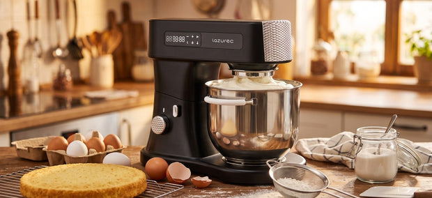 Lazurec Bakara Mix ONE Küchenmaschine mit luftig aufgeschlagener Biskuitmasse, daneben ein goldener Biskuitboden und Eier