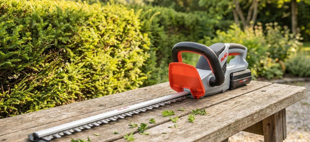 AL-KO Akku-Heckenschere HT 4055 auf einer Gartenbank vor frisch geschnittener Hecke