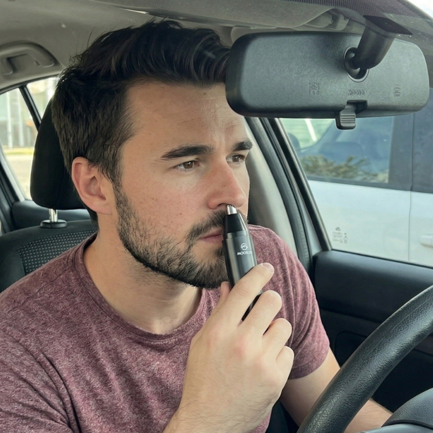 Mann verwendet einen elektrischen Nasenhaartrimmer im Auto während er auf dem Fahrersitz sitzt.