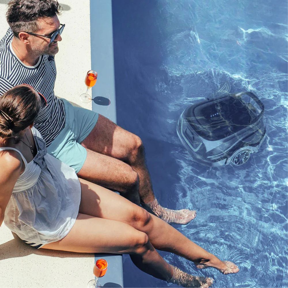 Paar sitzt entspannt am Poolrand, während ein automatischer Poolreiniger im Wasser arbeitet.